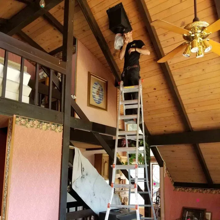 Person on a ladder fixing a ceiling light in a wood-paneled loft interior