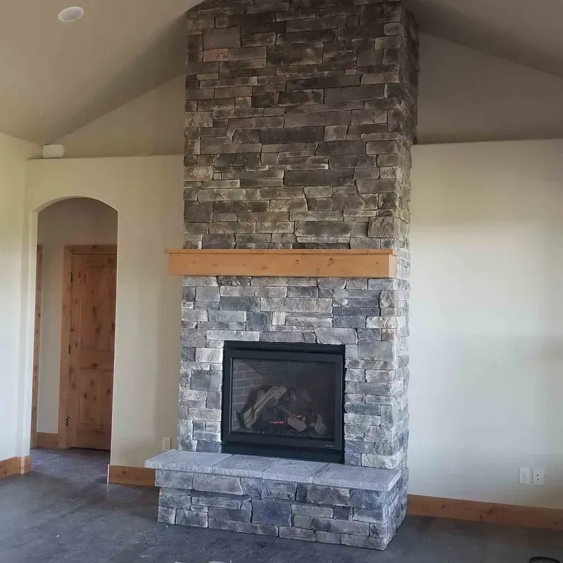 Living room with a tall stone fireplace and wooden mantel beneath a vaulted ceiling