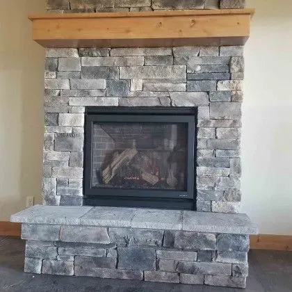 Stone fireplace with a black insert and wooden mantel in a living room
