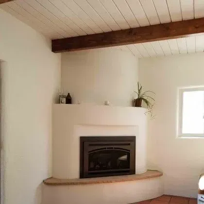 Cozy living room corner with white fireplace, wood beam ceiling, and small window.