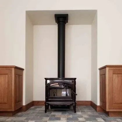 Black wood-burning stove centered in a white fireplace alcove with wood cabinets on both sides