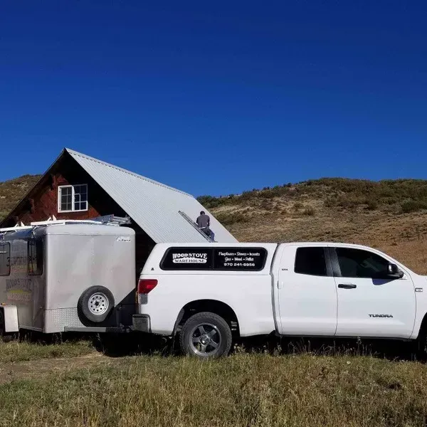 White pickup truck towing a silver camper trailer in a grassy field under a clear blue sky