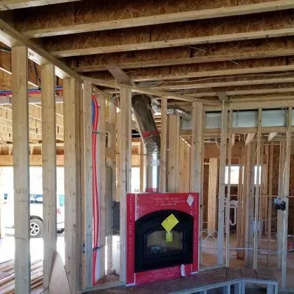 Framed interior under construction with exposed wood beams and a red fireplace unit in the center.