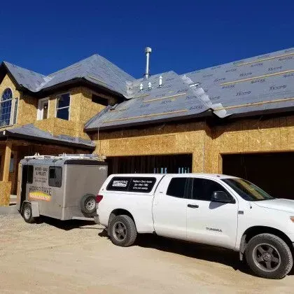 New house under construction with two parked trucks in front under a clear blue sky