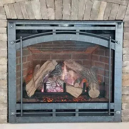 Lit fireplace with glowing embers, logs, and a black metal safety screen in a brick surround