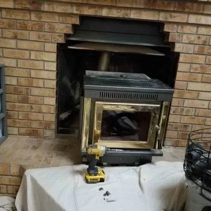 Brick fireplace with a metal insert being installed, a drill and tools on a white cloth in front.
