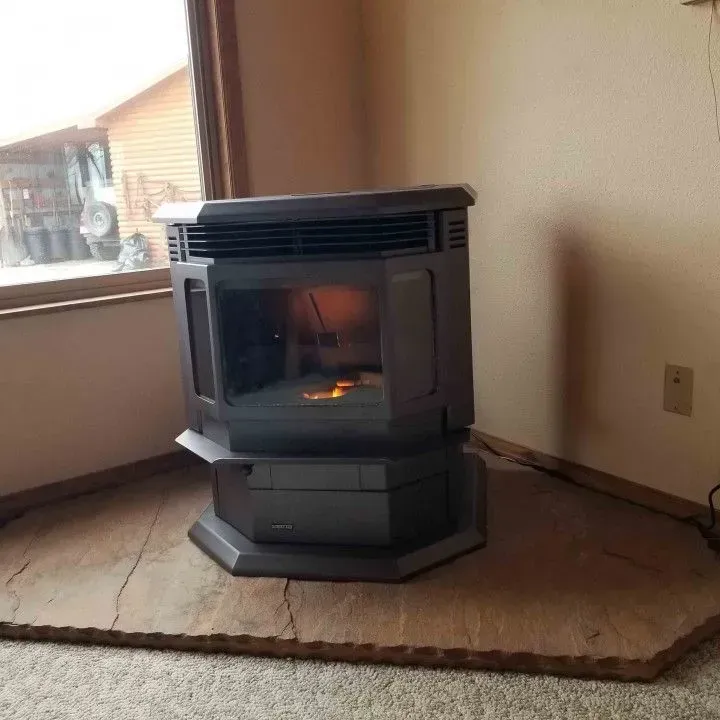 Black freestanding fireplace on carpeted floor beside a window in a sparsely furnished room