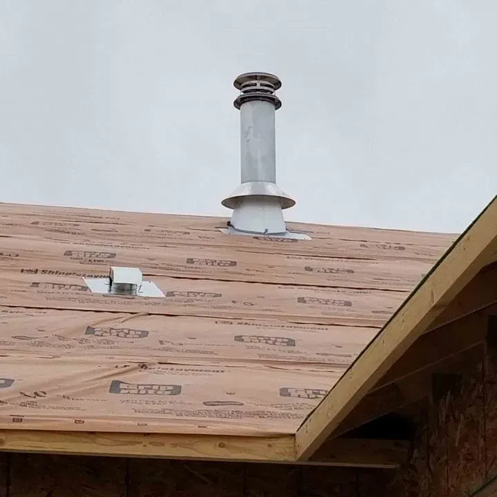 Partially roofed house with exposed sheathing, a vent pipe, and a small roof vent under an overcast sky