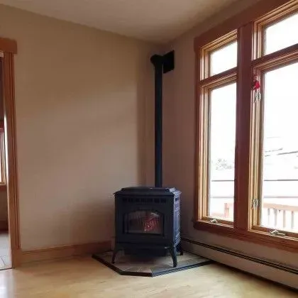 Small room with a black wood stove, beige walls, and tall wooden-framed windows.