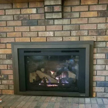 Brick fireplace with a gray-framed glass insert and burning logs.