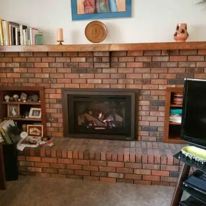 Brick fireplace with a lit fire, books, framed art, and decor on the mantel in a living room.