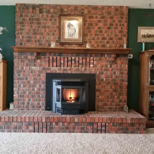 Brick fireplace with lit insert, wooden mantel, and framed picture in a carpeted living room