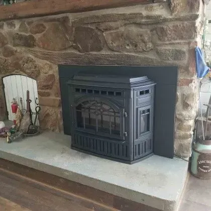 Black fireplace insert in a stone hearth with a concrete mantel.