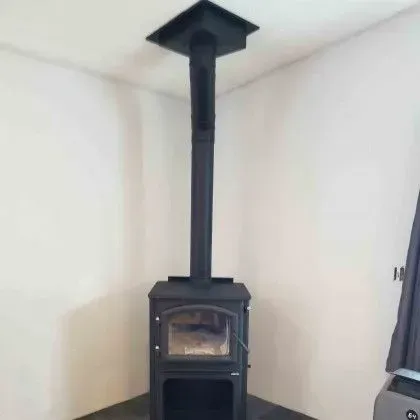 Black wood-burning stove with chimney pipe in a white corner room