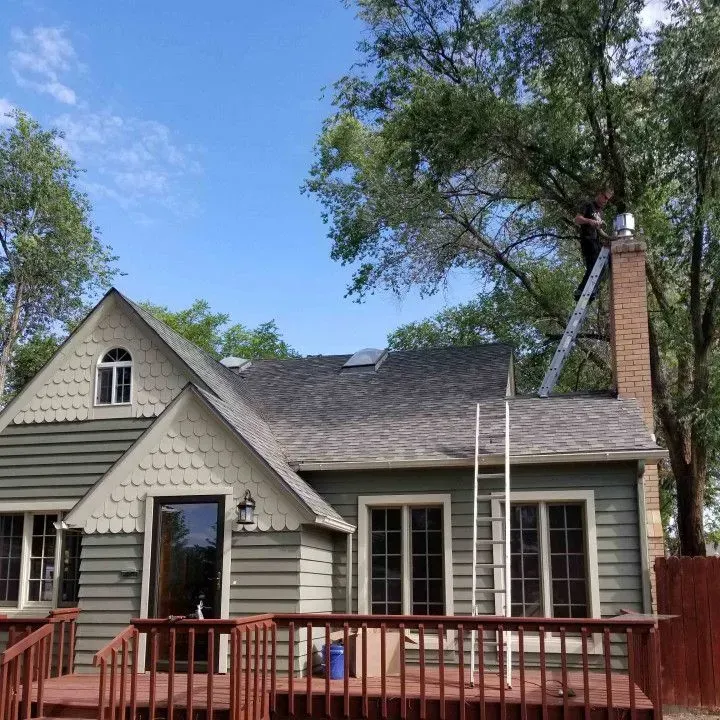 Gray house with red deck, tall trees, and blue sky