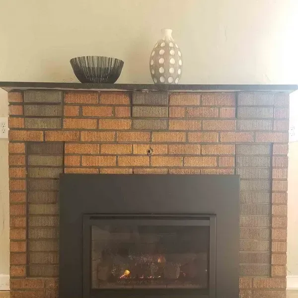 Brick fireplace with a dark metal insert and two decorative vases on the mantel.