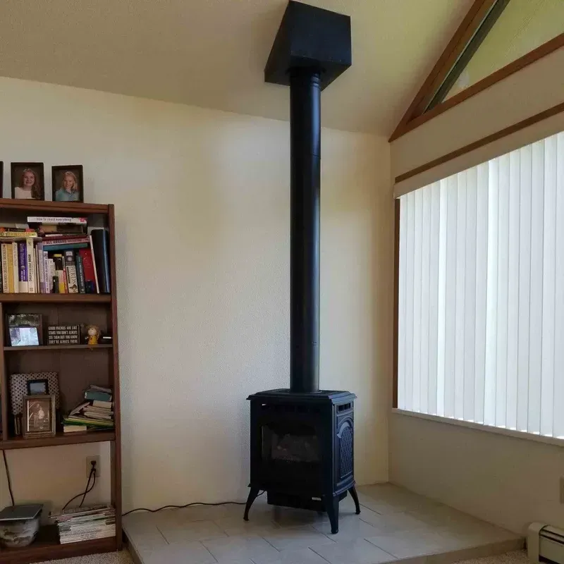 Living room with a black wood stove, tall chimney, bookshelf, and window blinds