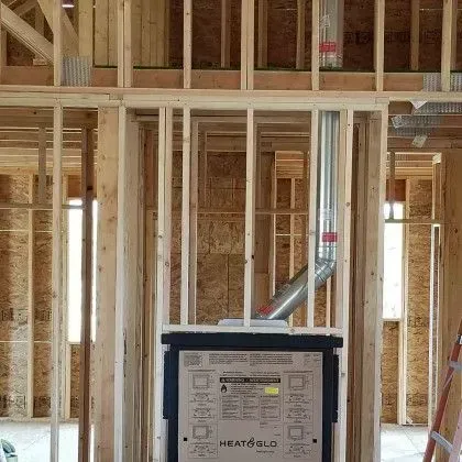 Framed house wall under construction with a black HVAC unit and silver ducting in the center.