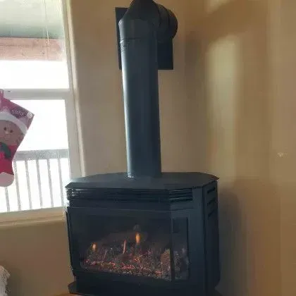 Black freestanding wood stove with a lit fire beside a window in a beige room