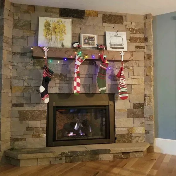 Stone fireplace with holiday stockings and decorations above a lit gas hearth