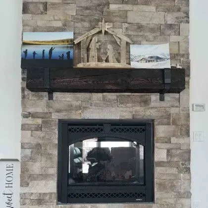 Stone fireplace wall with black mantel, framed photos, and a glass-front firebox
