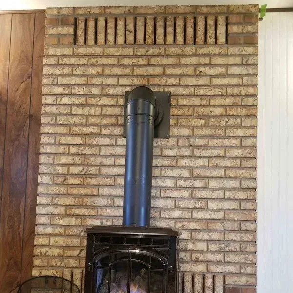 Brick fireplace with a black wood stove and blue stovepipe against a tan wall