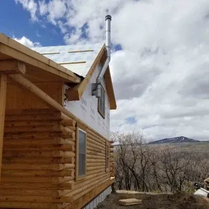 Wooden cabin exterior with a chimney under a partly cloudy sky, overlooking a barren landscape