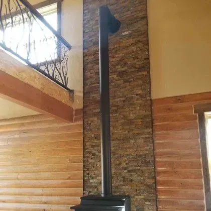 Tall black stove and chimney against a stone wall in a wood-paneled room