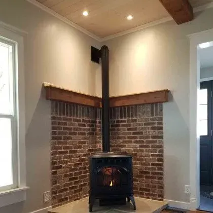 Brick corner fireplace with a black wood stove in a beige room with white trim and wood ceiling beams