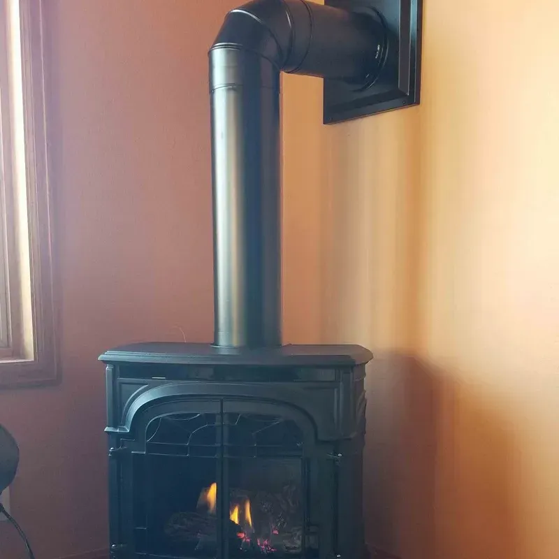 Black wood stove with a small fire and a vertical flue in a room by a window