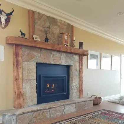 Living room fireplace with stone surround, wooden mantel, and fire burning in the hearth
