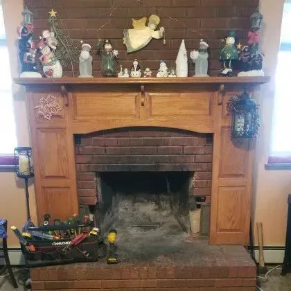 Wooden fireplace mantel with holiday figurines and decorations above a brick hearth