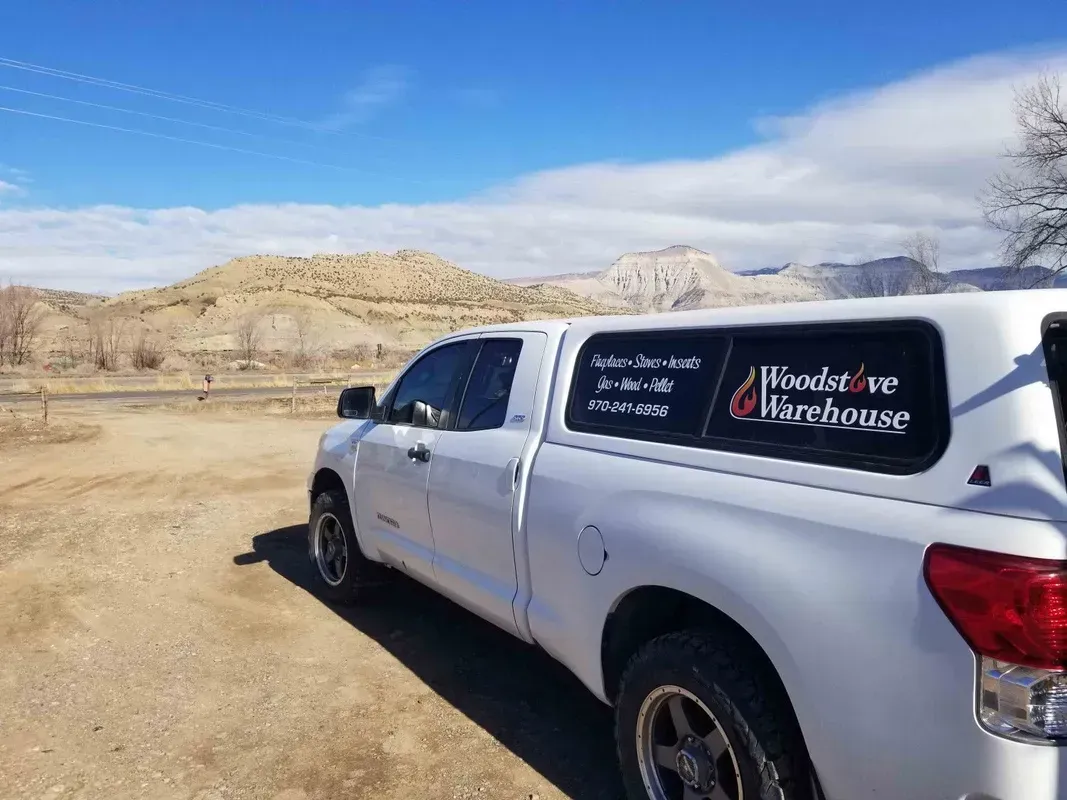 White pickup truck with a dark window decal parked on a dirt road in a desert landscape under a blue sky