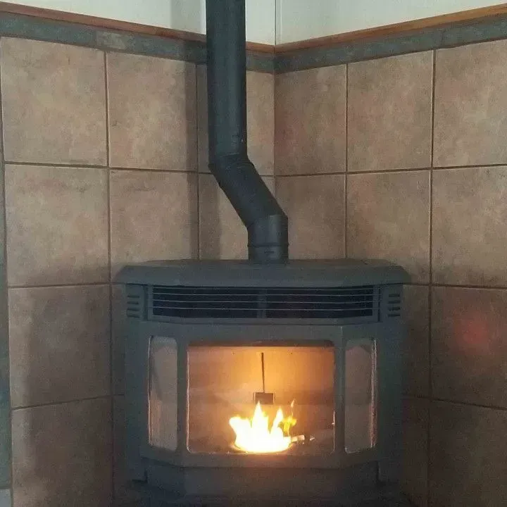 Black wood stove with a visible flame against tan tiled walls.