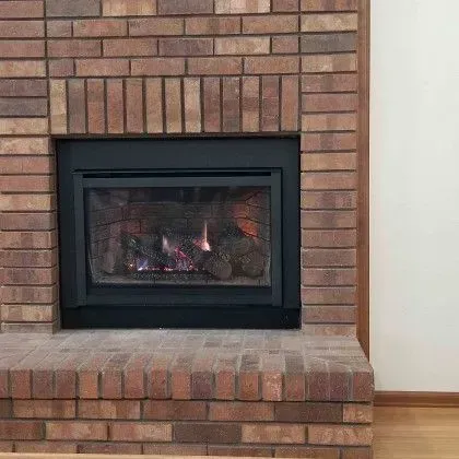 Brick fireplace with a lit black insert and brick hearth in a room with wood flooring