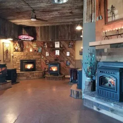 Warm rustic room with several lit wood stoves, stone hearths, and wood-paneled walls.