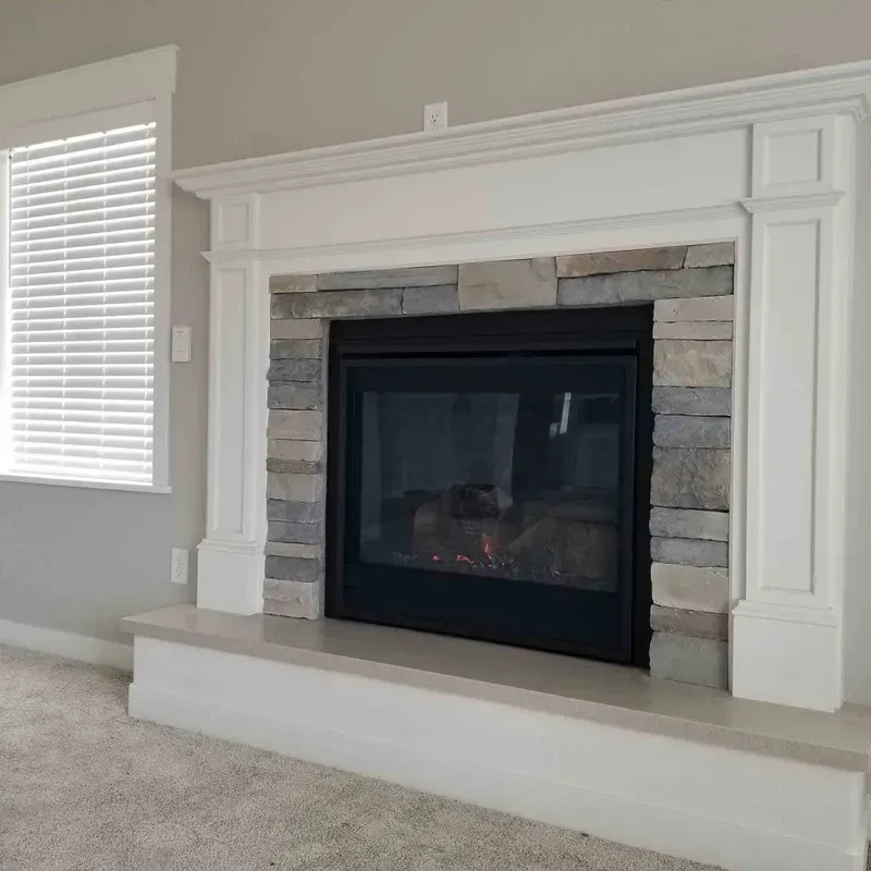 White fireplace with black insert and stone surround in a carpeted living room