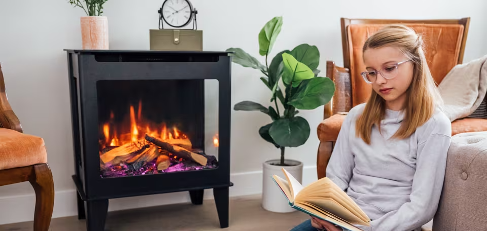 Woman reading beside a lit electric fireplace in a cozy living room