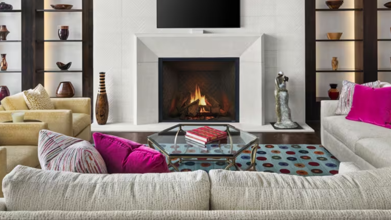 Modern living room with fireplace, neutral sofas, colorful pillows, and a glass coffee table