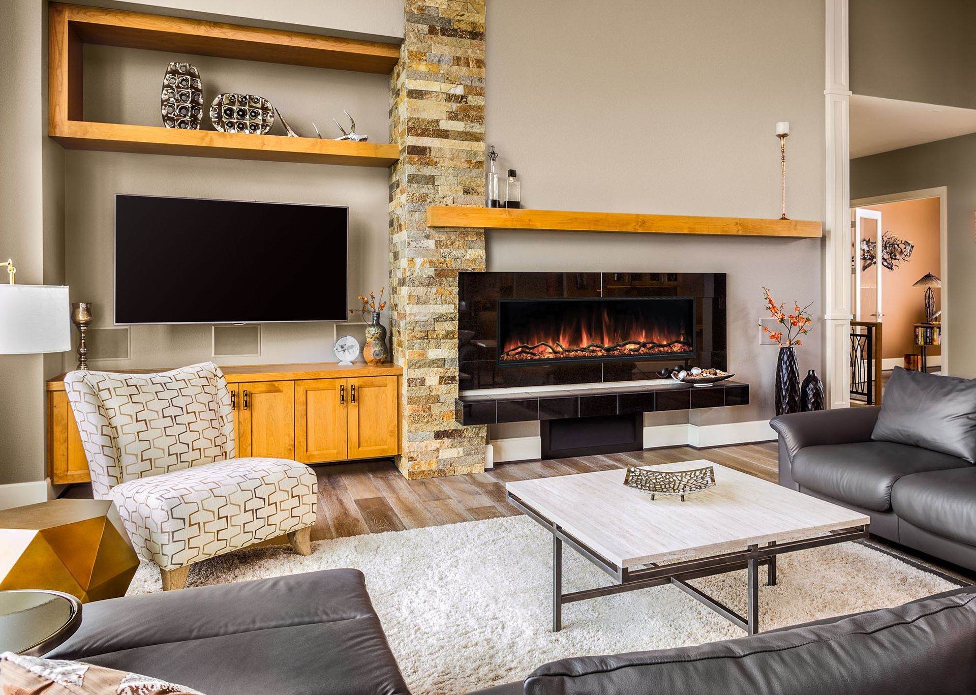 Cozy living room with wood stove, wall clock, and baskets of firewood next to a kitchen.