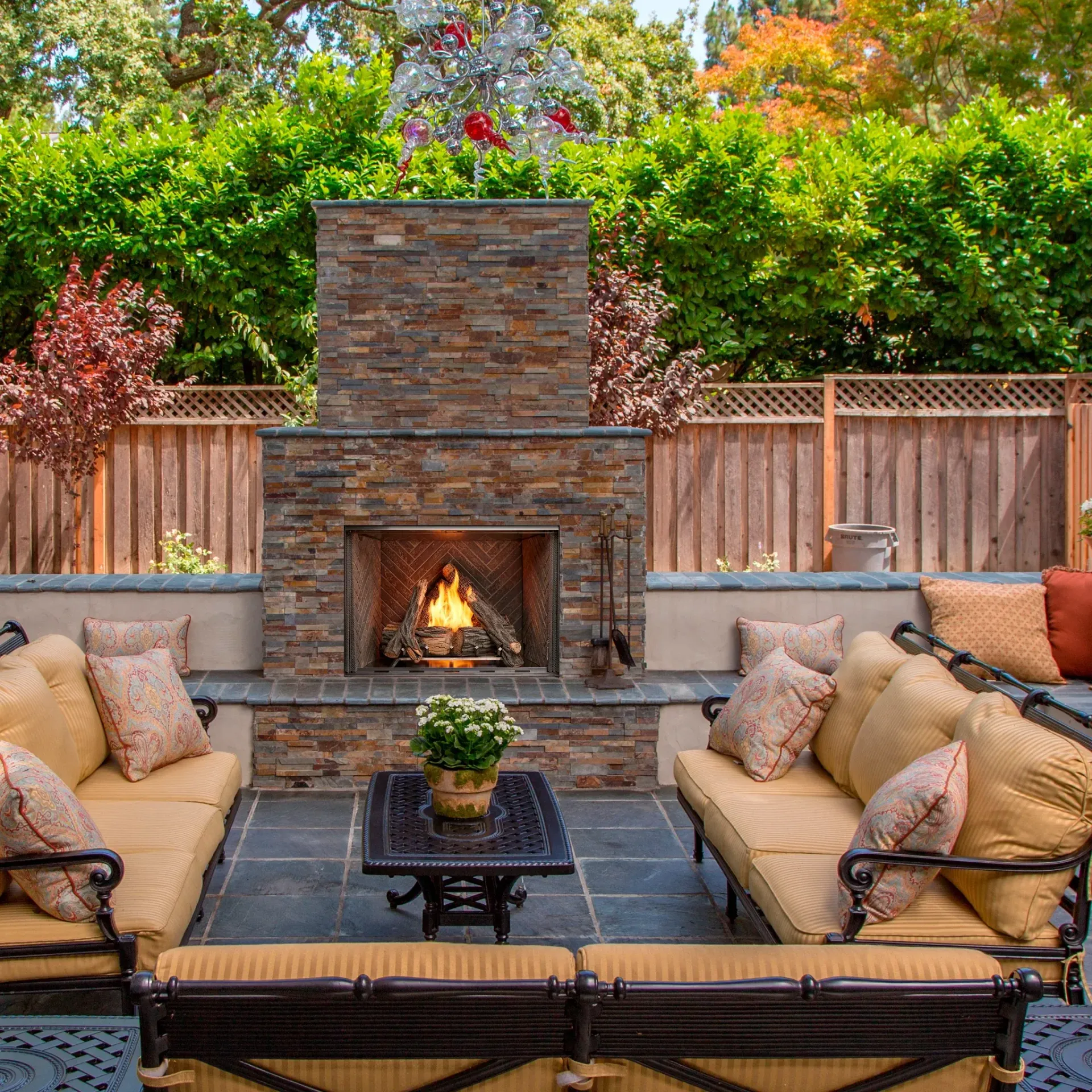 Outdoor patio with stone fireplace, cushioned chairs, and wooden coffee table on patterned rug