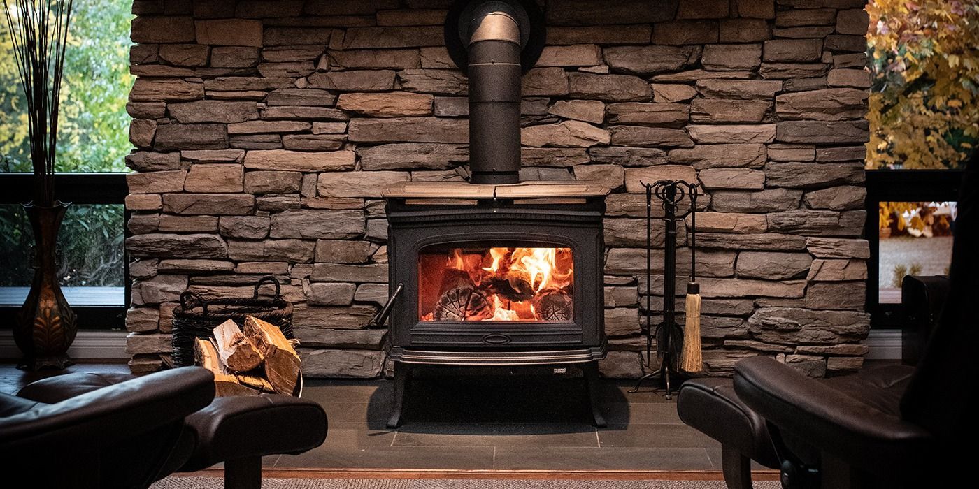 Warm rustic room with several lit wood stoves, stone hearths, and wood-paneled walls.