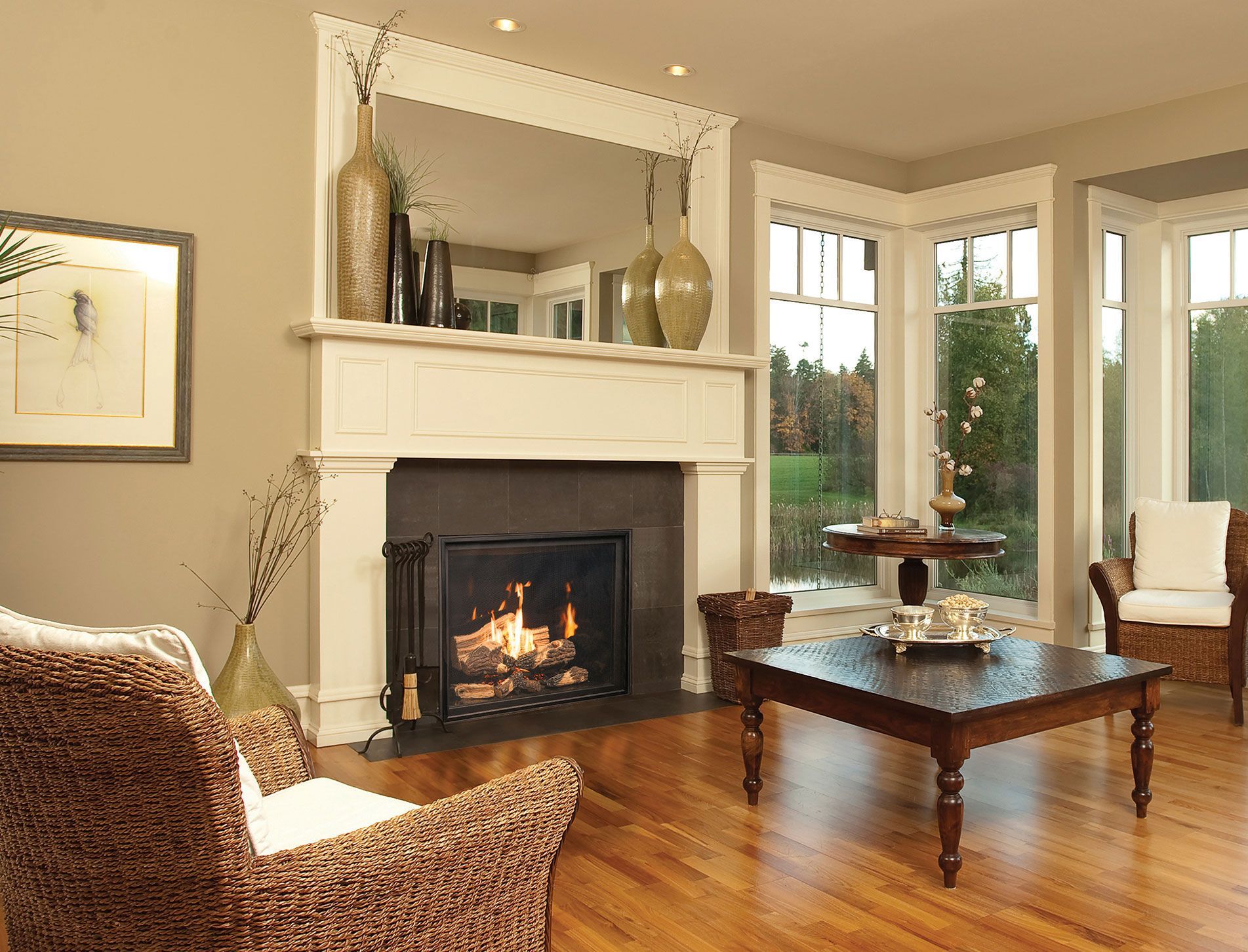 Cozy living room with fireplace, mirror mantle, hardwood floors, and large windows with natural light