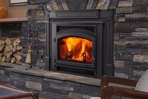 Stone fireplace with a black insert burning bright orange flames, stacked firewood on the left.