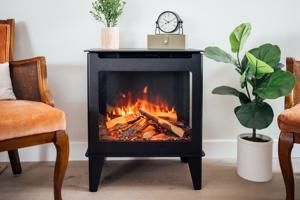 Black electric fireplace with flames, flanked by a brown chair and a potted plant in a bright room