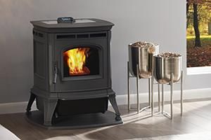 Black wood-burning stove with visible flame beside two metal ash bins on stands in a bright room