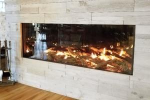 Modern linear gas fireplace set into a light stone wall with visible flames and a wooden floor nearby