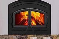 Black wood-burning fireplace with a bright orange fire behind a glass door
