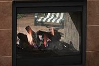 Lit fireplace with glowing logs behind a glass screen in a dark tiled surround