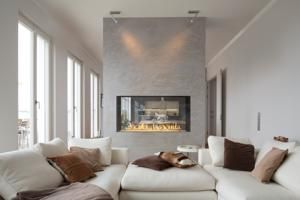 Bright modern living room with a white sectional sofa and a central stone fireplace with flames.